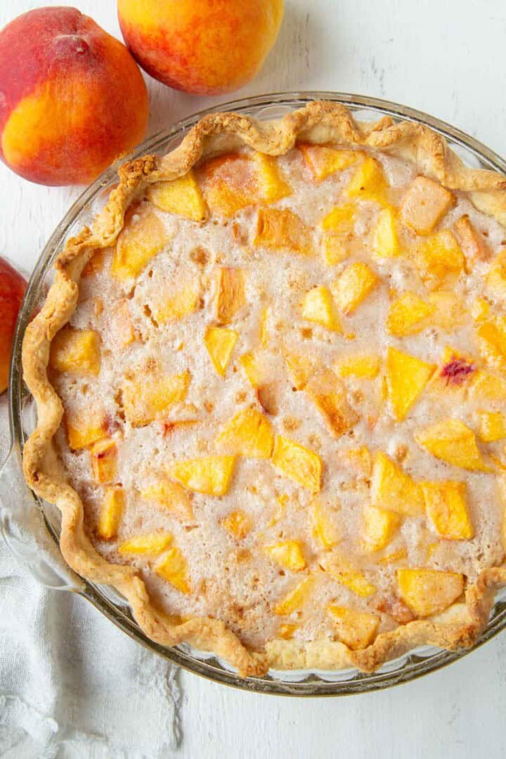 whole peach cream pie next to a couple fresh peaches.
