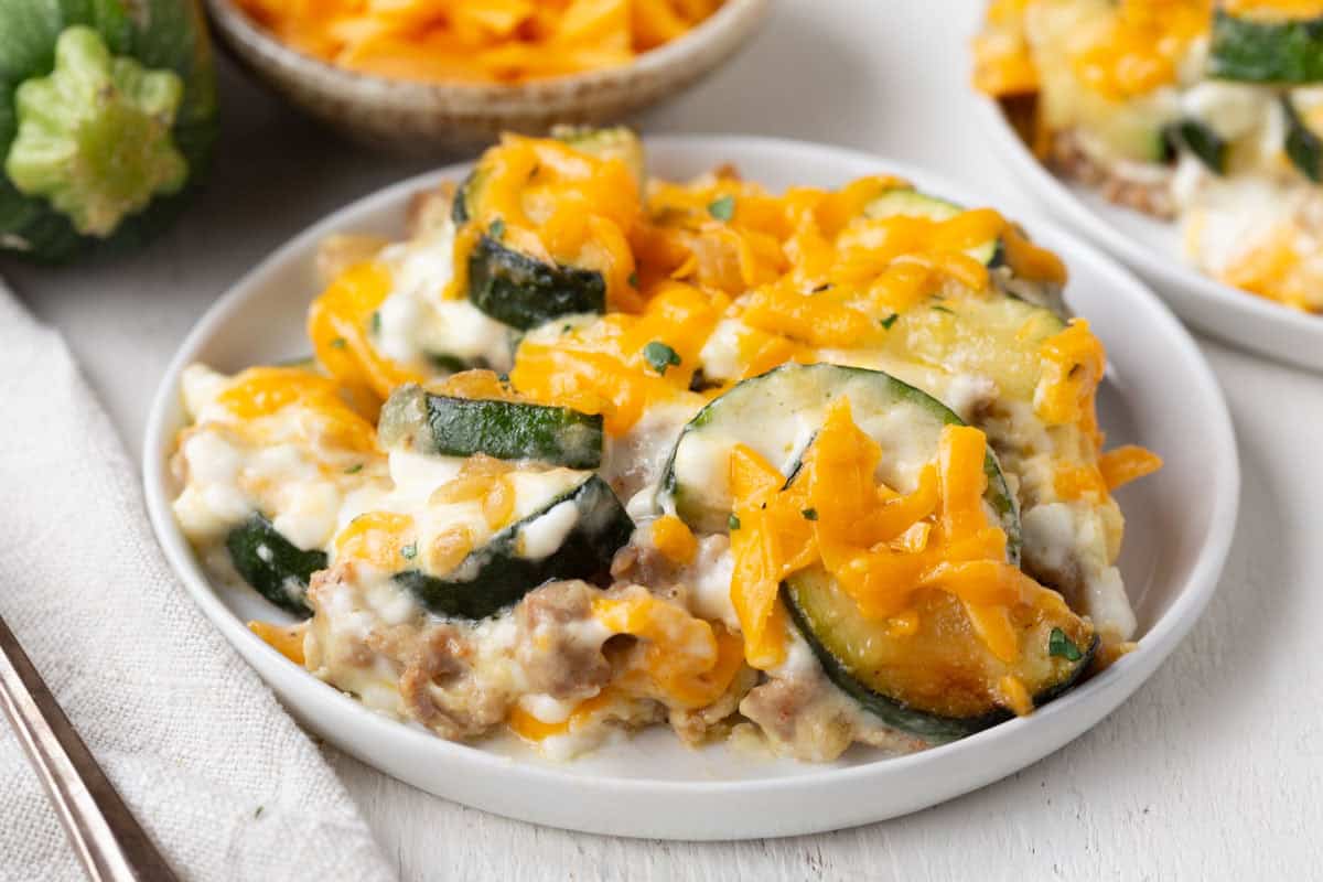 italian sausage and zucchini casserole topped with cheese on a white plate.
