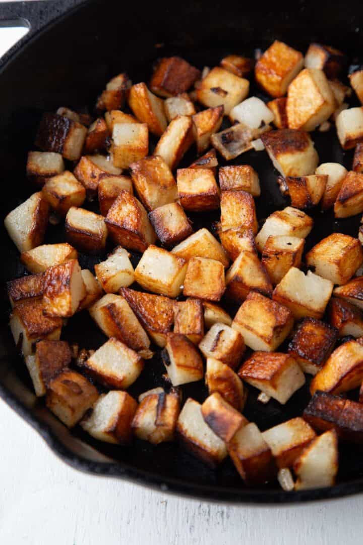 cast iron skillet filled with crispy home fried potatoes cut into cubes.