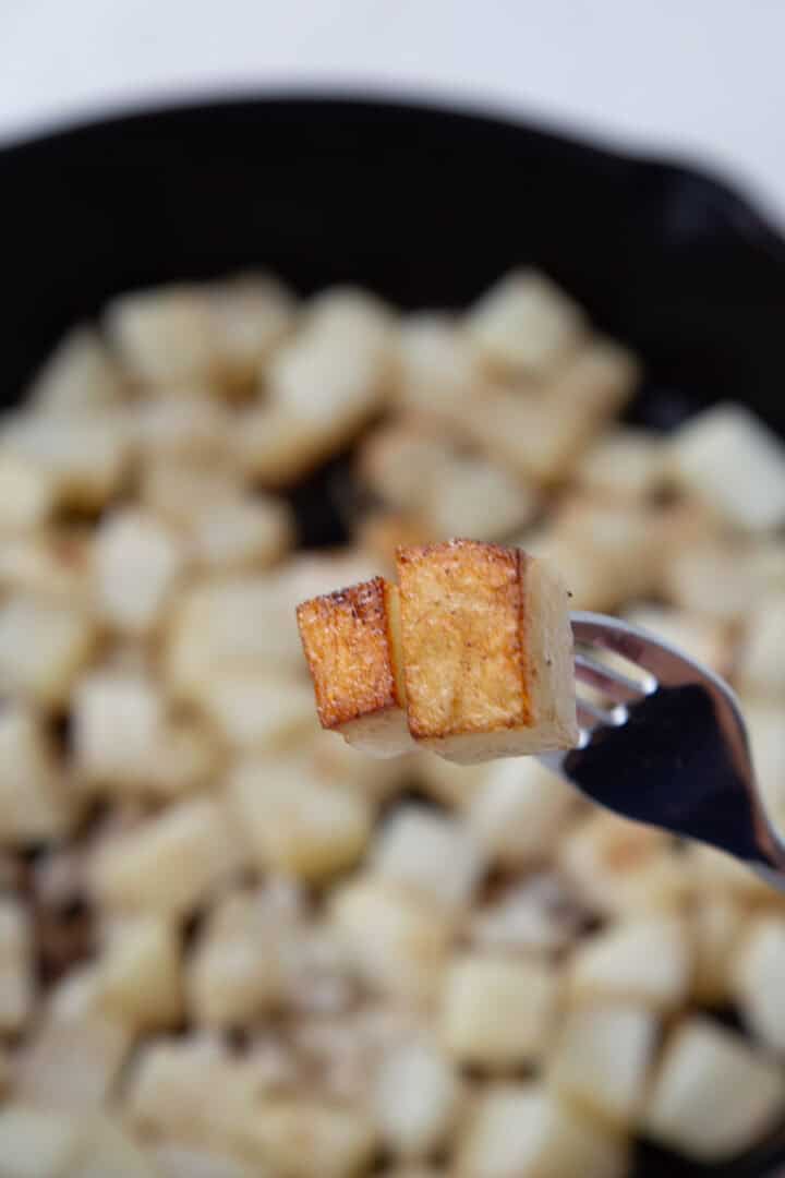 two cubes of potatoes that are crispy on the bottom being held up with a fork.