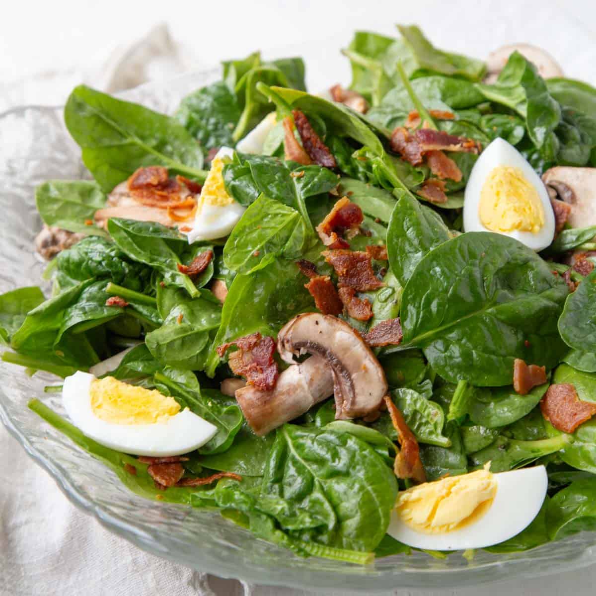 baby spinach with hard boiled eggs, mushrooms, and crispy bacon pieces in a hot bacon dressing.