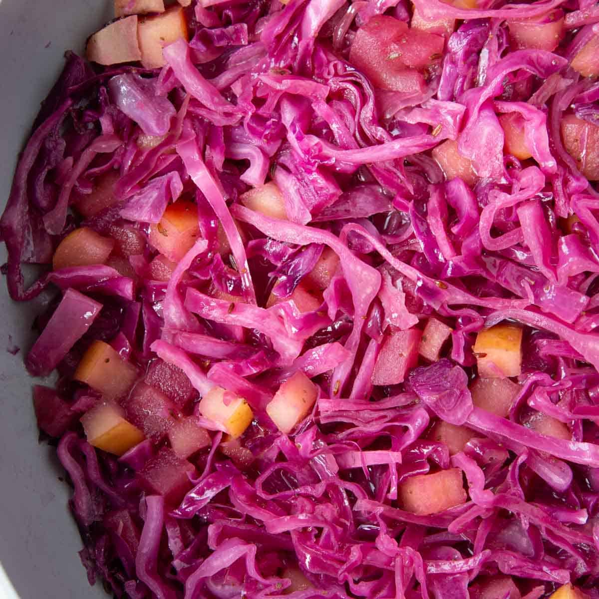 sweet and sour purple cabbage in a pan with pieces of apples.