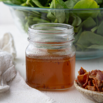 hot bacon salad dressing in a mason jar next to a pile of crumbled bacon.