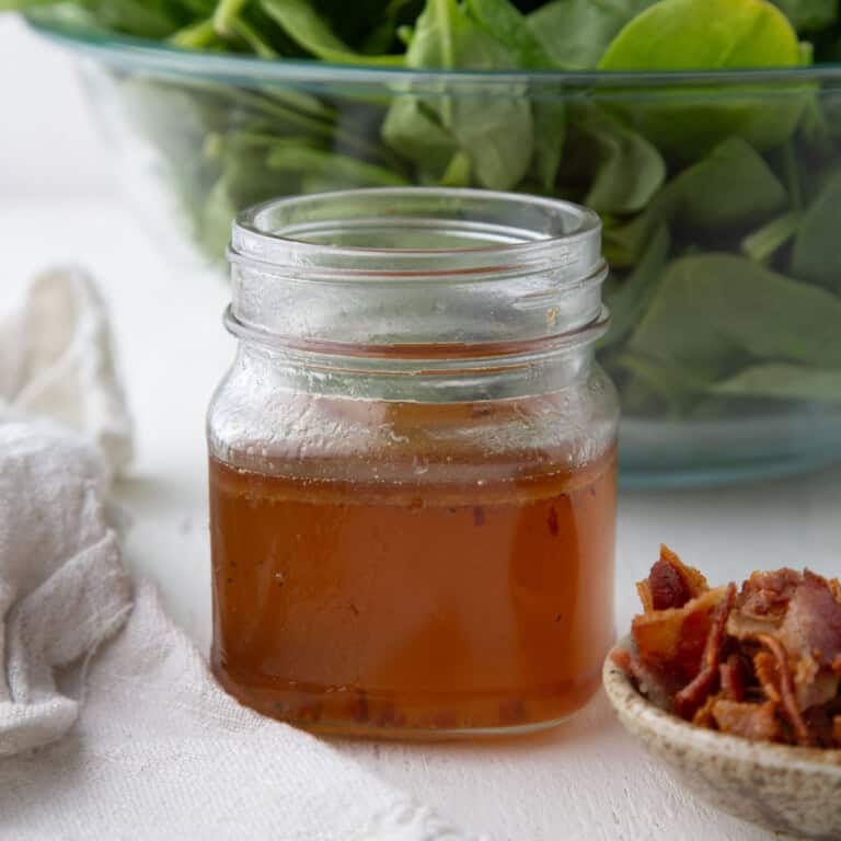 hot bacon salad dressing in a mason jar next to a pile of crumbled bacon.