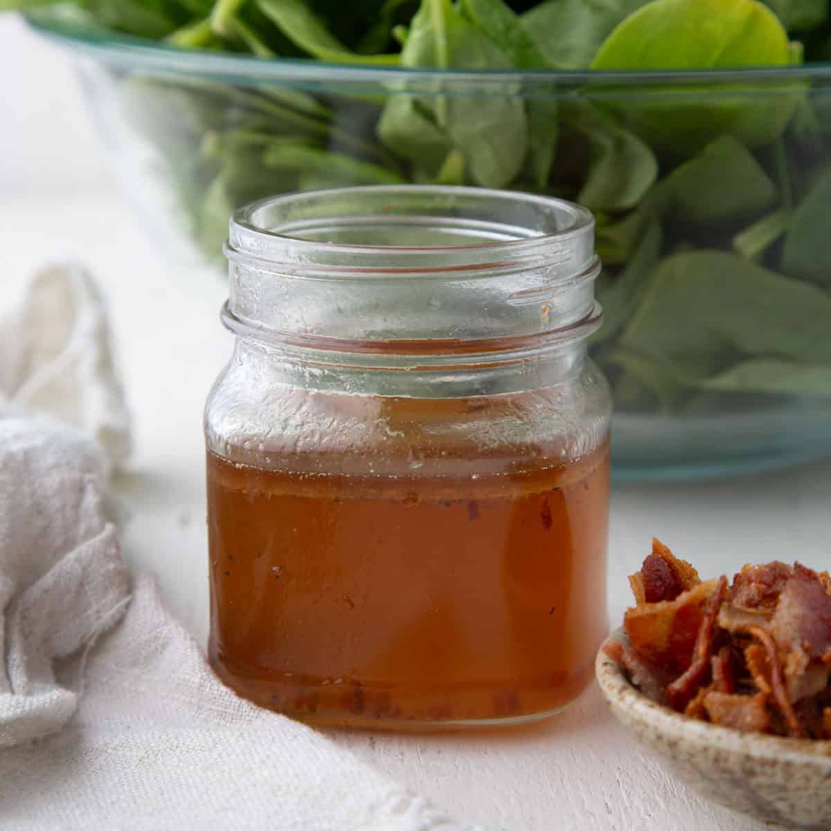 hot bacon salad dressing in a mason jar next to a pile of crumbled bacon.