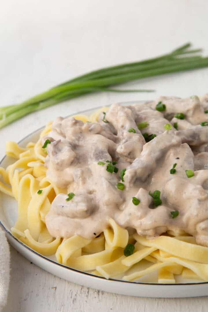 strips of beef in a creamy onion soup mix sauce on top of egg noodles on a plate.
