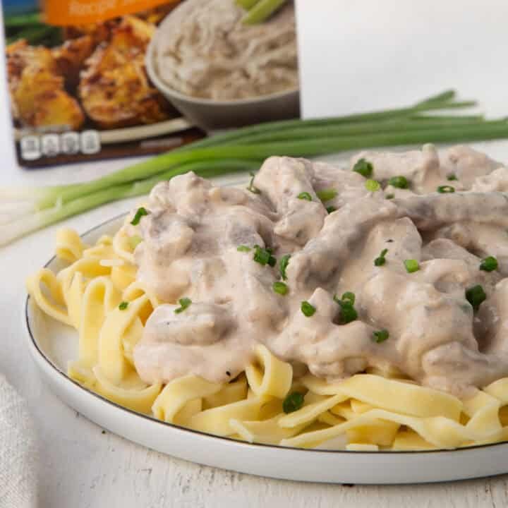 beef stroganoff on a plate over egg noodles with a box of onion soup mix behind it.