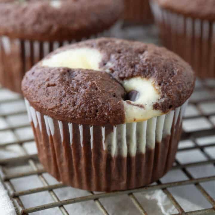 black bottom cupcake with chocolate cake and a cream cheese swirl sitting on a wire rack.