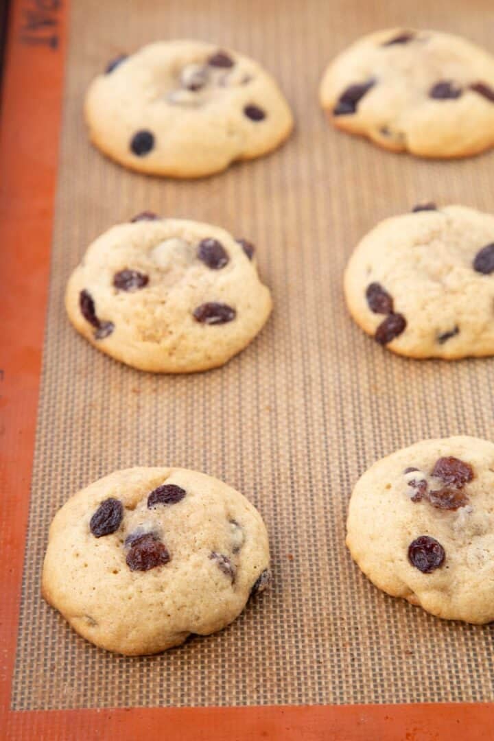 baked hermit cookies topped with raisins on a baking sheet.