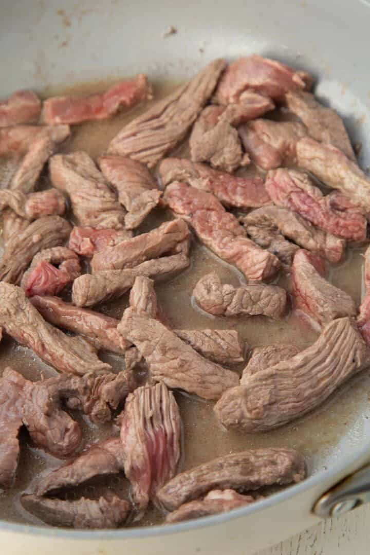 top sirloin strips cooking in a skillet.
